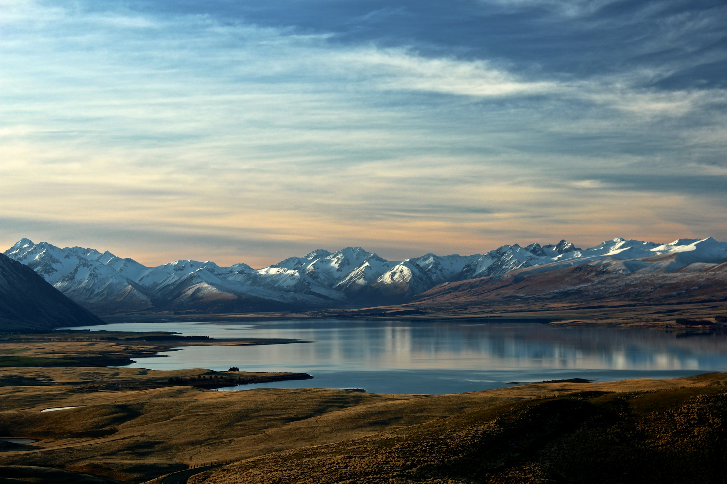 Lake Tekapo at dusk, mountains in the distance, the horizon wide.
