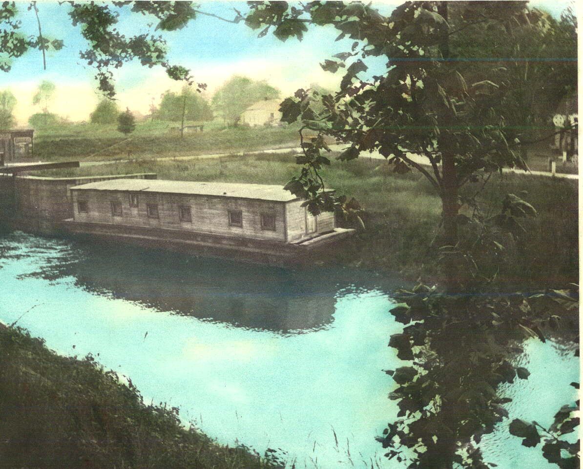 A canal boat passing through Lock 13 of the Miami and Erie Canal at Defiance, Ohio, approximately 1900 — lock gates closed behind, water held at the upper level, the boat waiting for the chamber to fill before it can move on. Toledo-Lucas County Public Library collection.